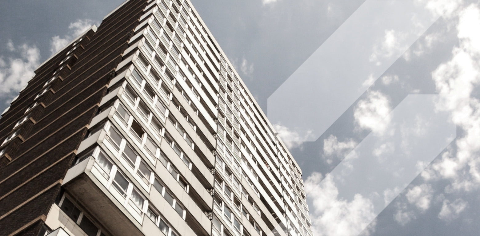 Tall building with a reflective surface showing geometric distortion and clouds.
