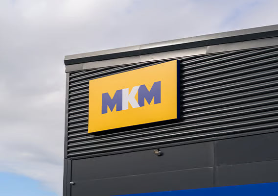 MKM logo on a building exterior with a cloudy sky background.